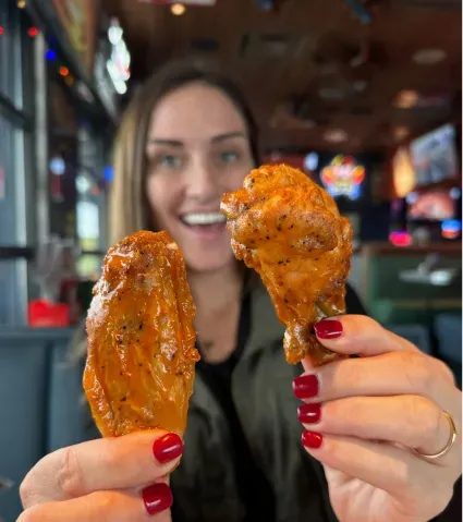 Girl holding two chicken wings up close